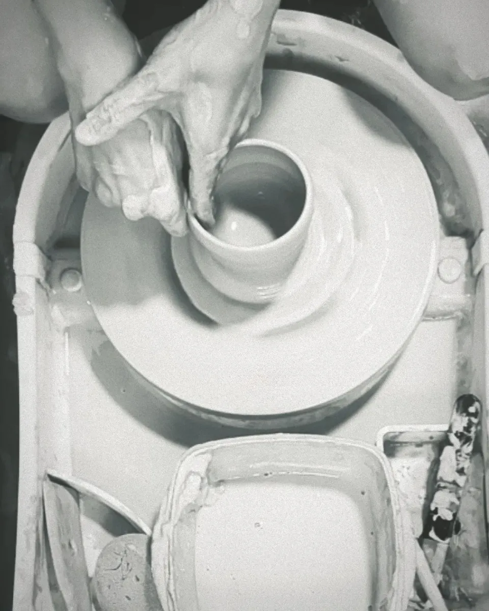 Hands shaping a clay vessel on the potter's wheel